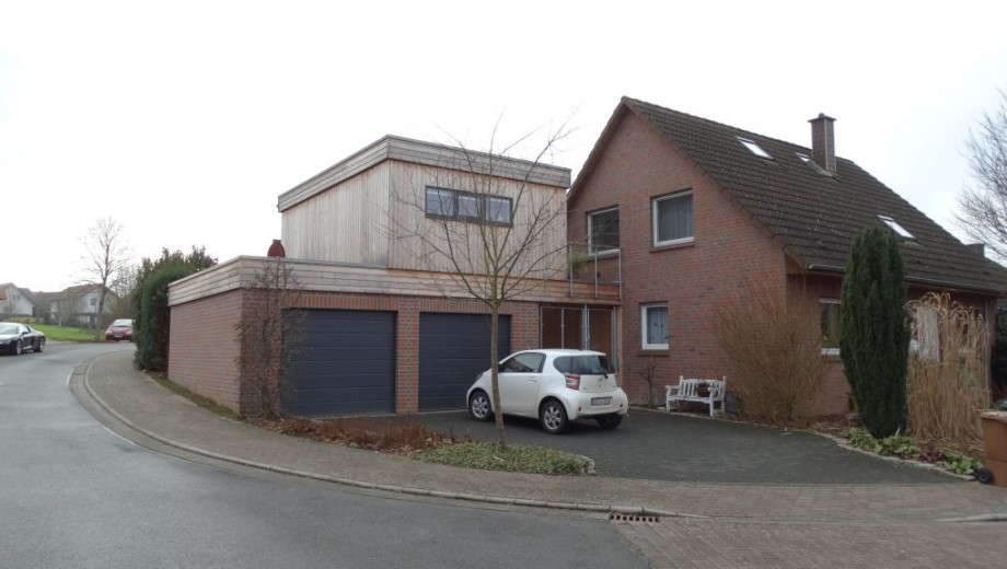 Modernes Wohnhaus mit rotem Backstein, Holz-Anbau, weißem Auto und kahlen Bäumen im Vorort.
