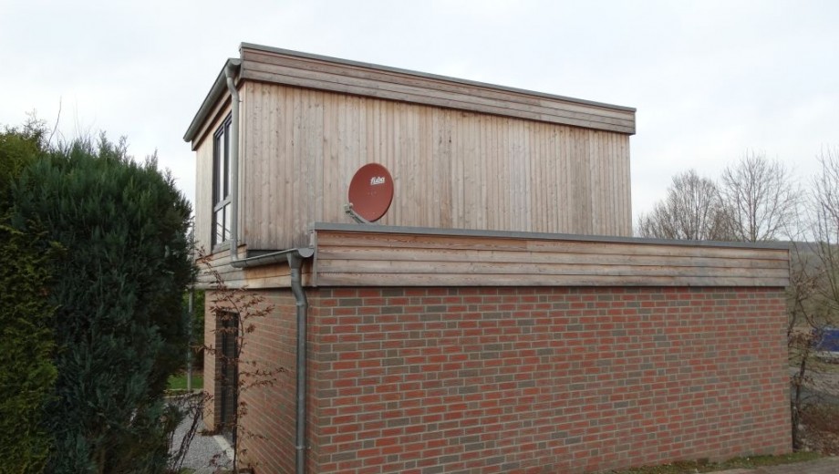 Modernes Gebäude mit Backstein- und Holzverkleidung, umgeben von Bäumen; bewölkter Himmel.