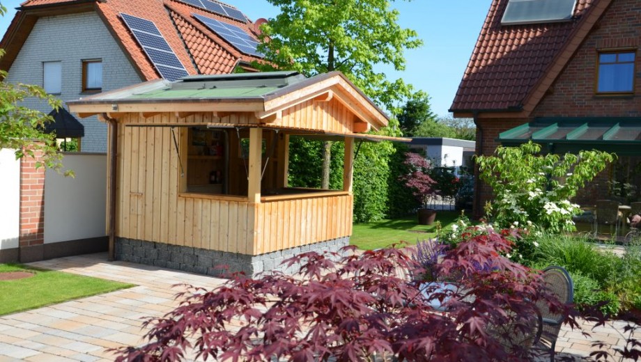 Gepflegter Garten mit Holzpavillon, Solarpaneelen auf Ziegeldächern und buntem Laubbaum im Vordergrund.