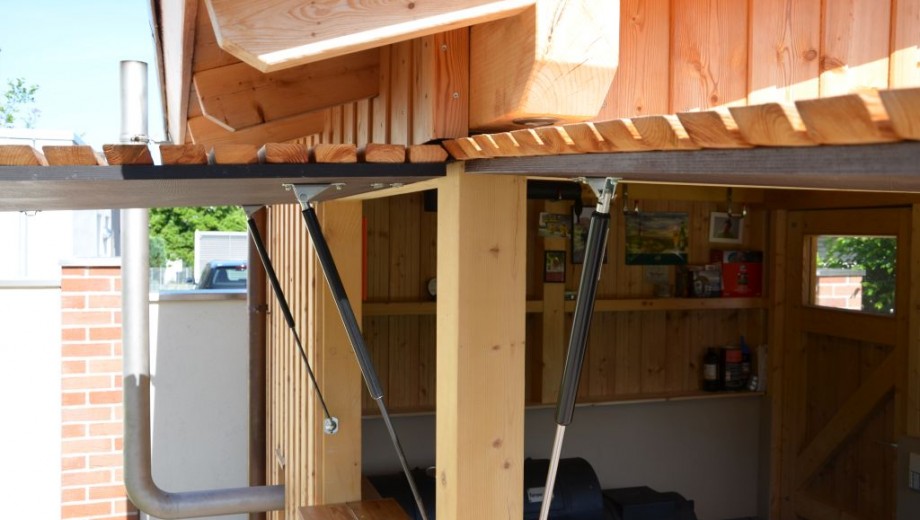 Ein gut organisierter Holzschuppen mit offenen Regalen, Werkzeugen und einem Ofenrohr.