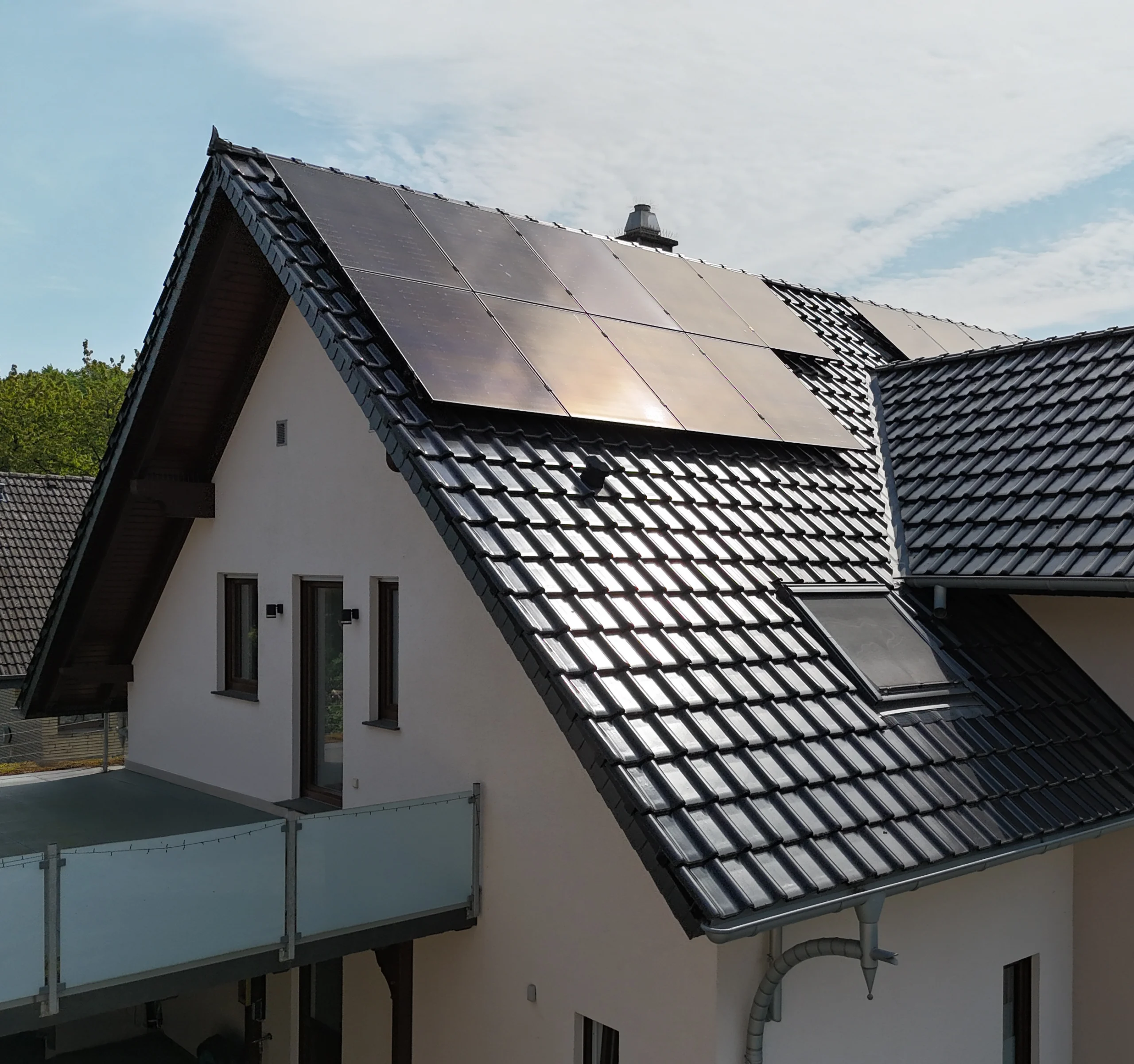 Modernes Wohnhaus mit geneigtem Dach, Solarpaneelen, Dachfenster und heller Fassade unter blauem Himmel.