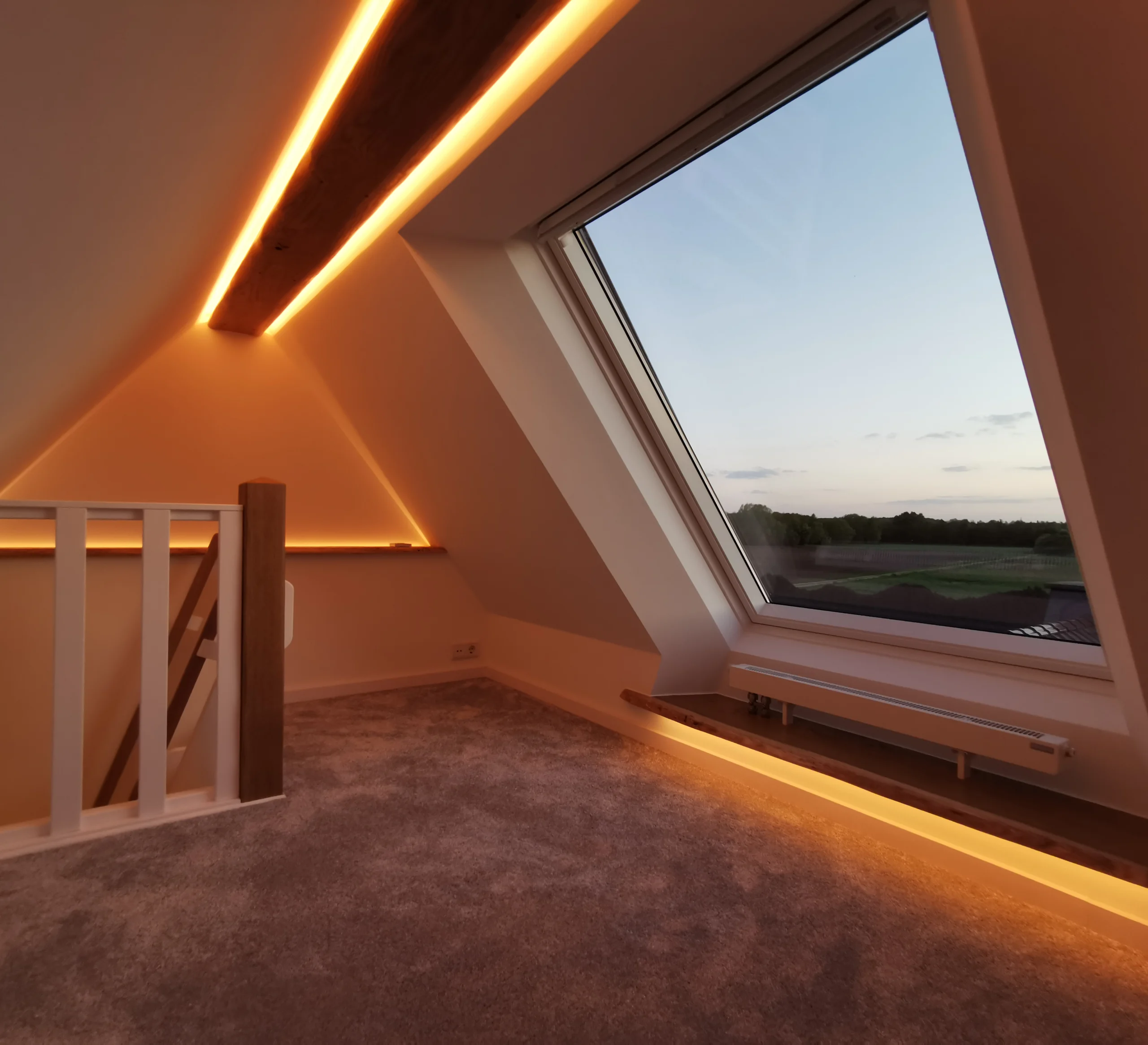 Moderner Dachboden mit großem Fenster, warm beleuchtet, Blick auf Landschaft und klaren Himmel.