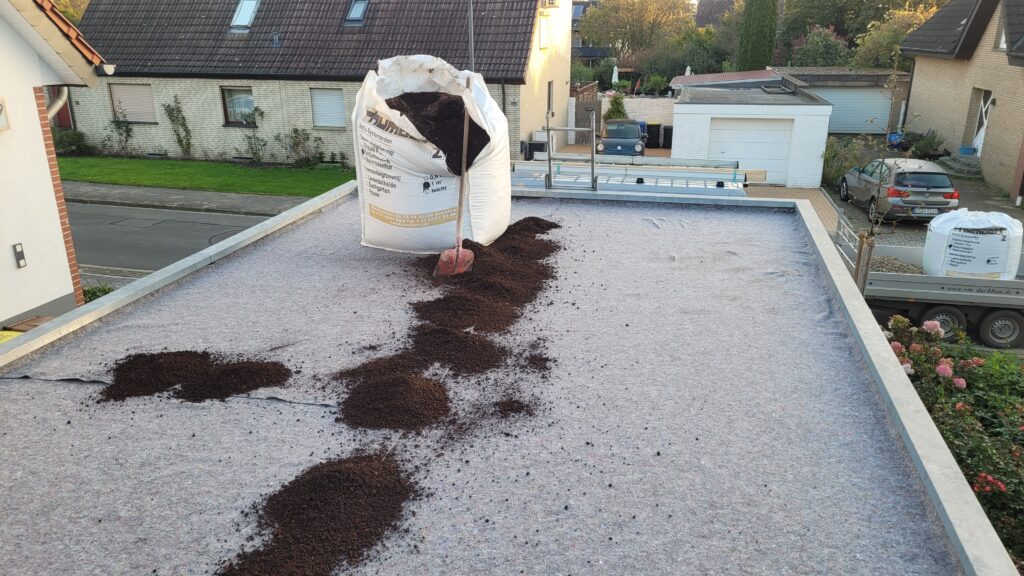 Ein großer Sack Erde wird mit einer Schaufel auf einem Flachdach verteilt, um ein Gründach anzulegen.