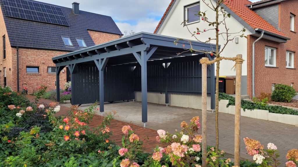 Moderner Carport vor Backsteinhäusern mit Solarpaneelen, umgeben von bunten Blumen.