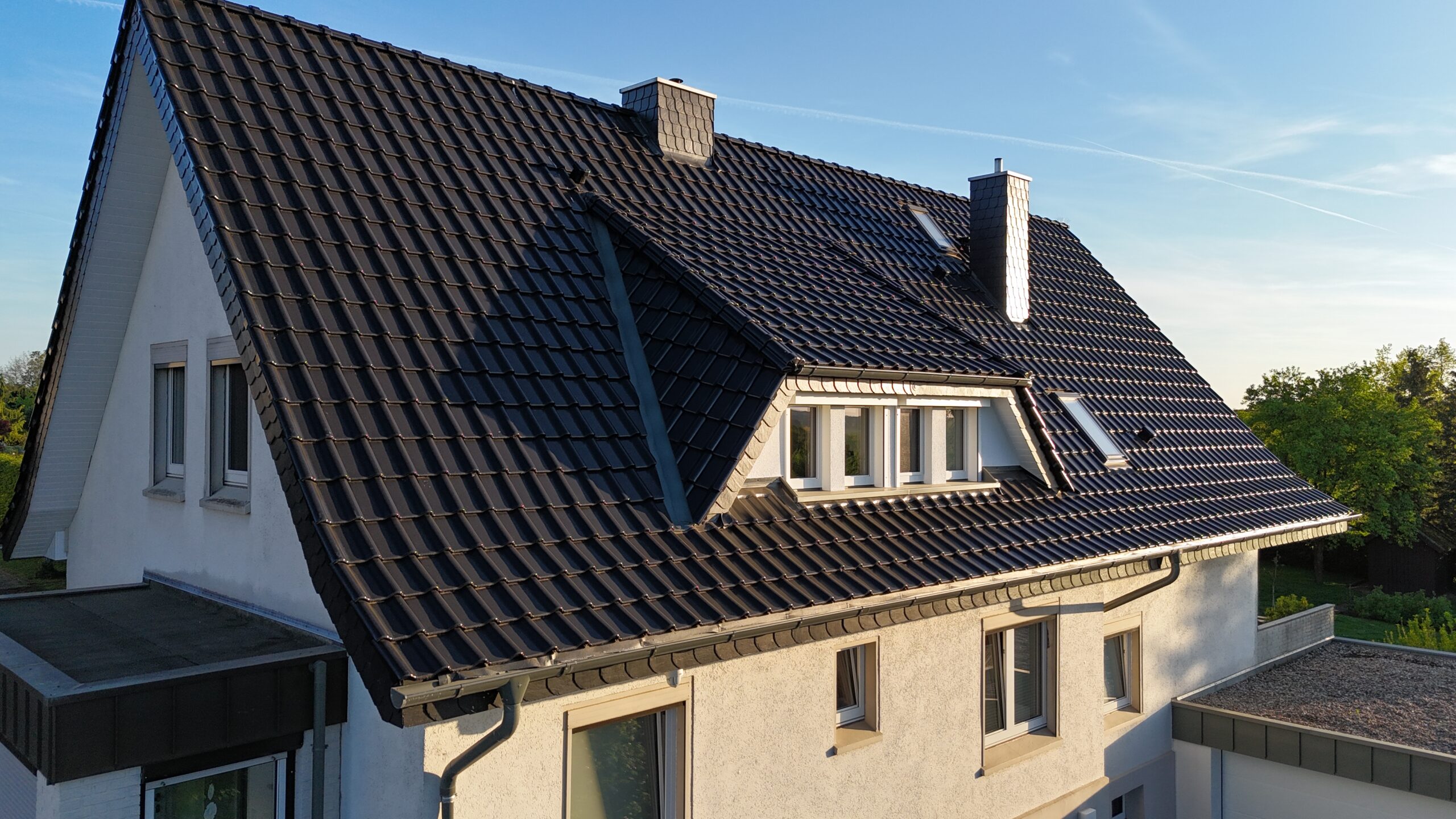 Zweistöckiges Haus mit steilem, dunkelgrauem Satteldach und heller Fassade unter klarem, blauem Himmel.
