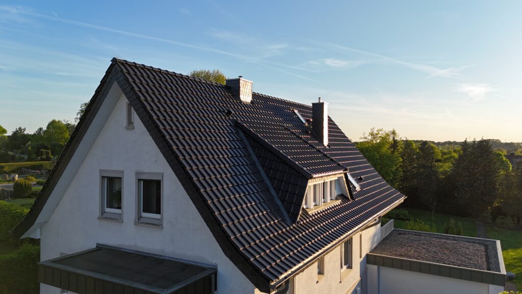 Vogelperspektive auf ein weißes Einfamilienhaus mit grauem Satteldach, umgeben von grüner Vegetation.