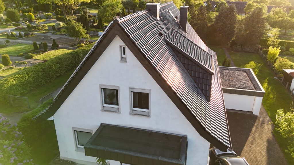 Vogelperspektive auf ein zweistöckiges Haus mit Satteldach, Garage und Auto, umgeben von grüner Natur.