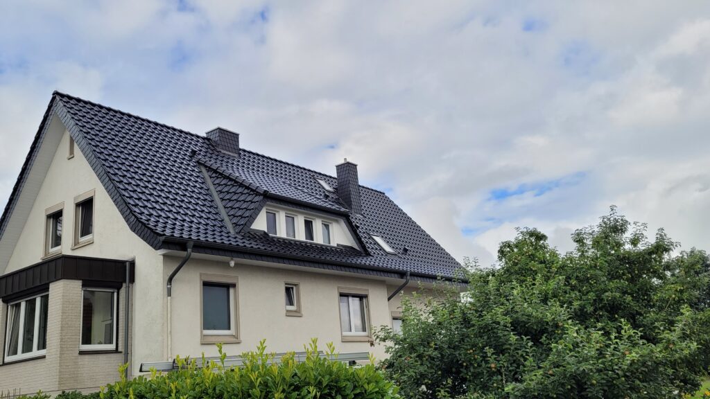 Ein ruhiges Wohnhaus mit steilem Dach, umgeben von grüner Vegetation unter teils bewölktem Himmel.