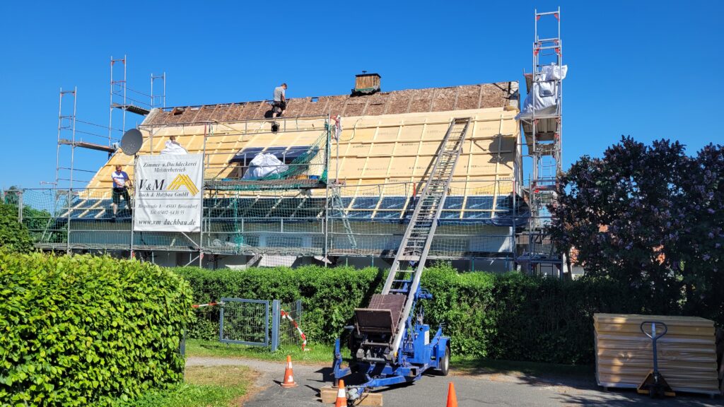 Baustelle mit Dacharbeiten: Arbeiter renovieren Dach, Schrägaufzug transportiert Materialien.
