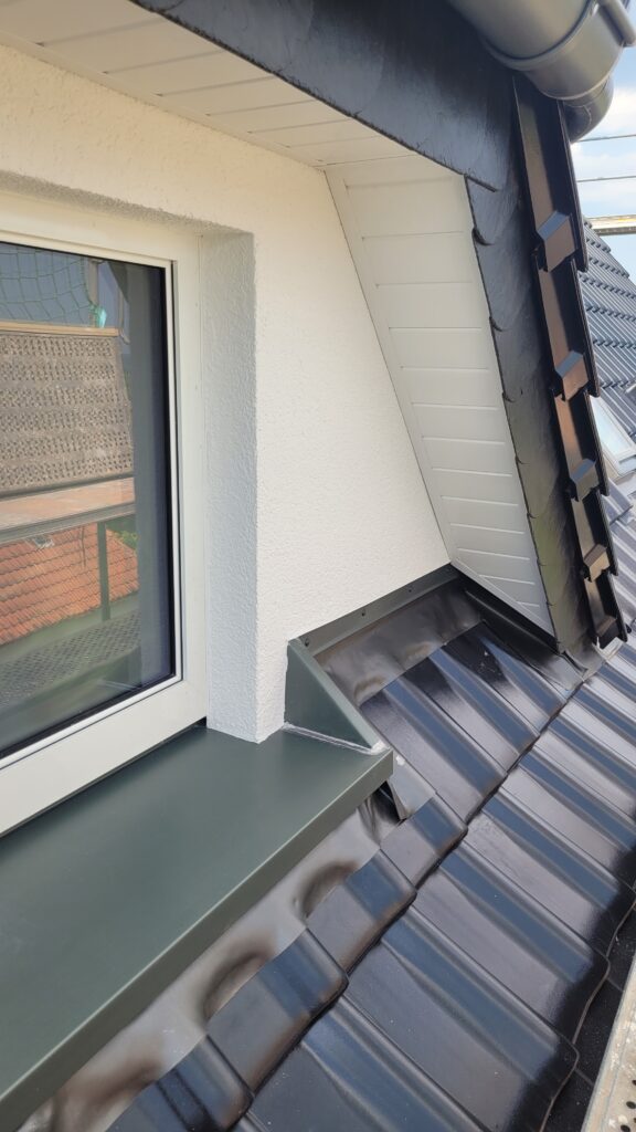Ein Dach mit dunklen Ziegeln, einem weißen Fenster und einer metallischen Dachrinne.