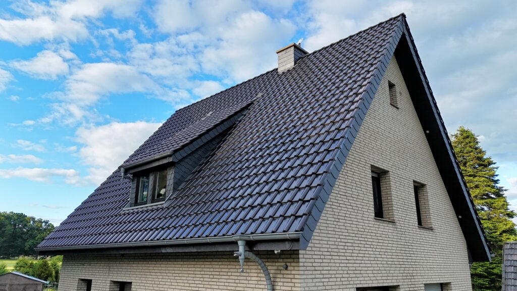 Einfamilienhaus mit steilem, dunkelgrauem Satteldach, helle Klinkerfassade und integriertem Dachfenster.