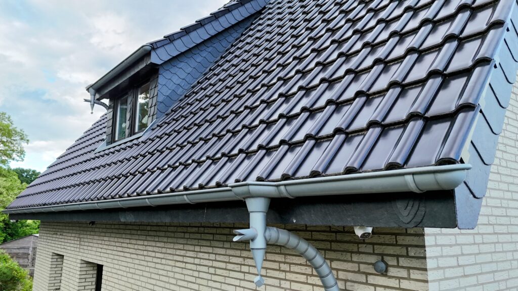 Ein modernes Hausdach mit dunkelblauen Ziegeln, grauer Dachrinne und integriertem Dachfenster.