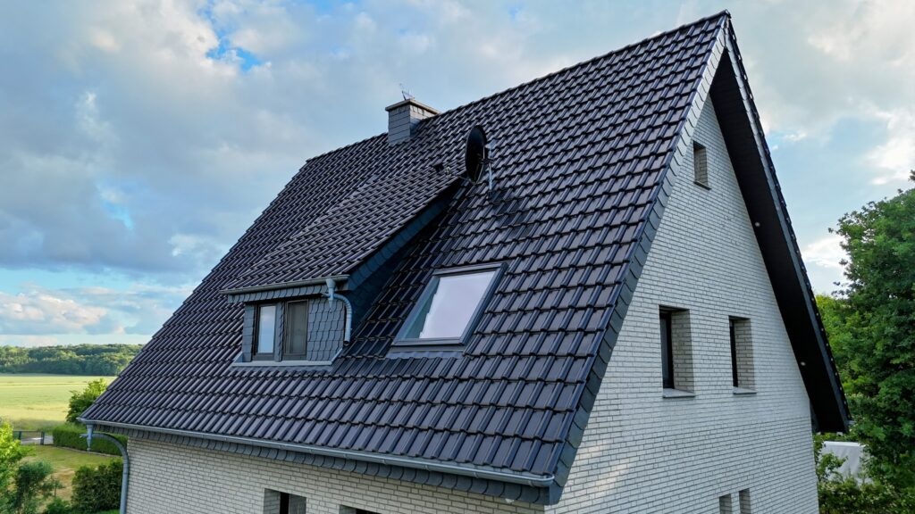 Einfamilienhaus mit spitzem Dach, umgeben von grüner Landschaft unter blauem Himmel mit Wolken.