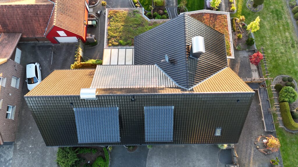 Luftaufnahme eines modernen Wohnhauses mit Solarpaneelen auf dem Dach, umgeben von Grünflächen.
