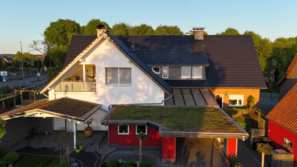 Modernes zweistöckiges Haus mit Satteldach, teils weiß, teils aus roten Backsteinen, umgeben von Grün.
