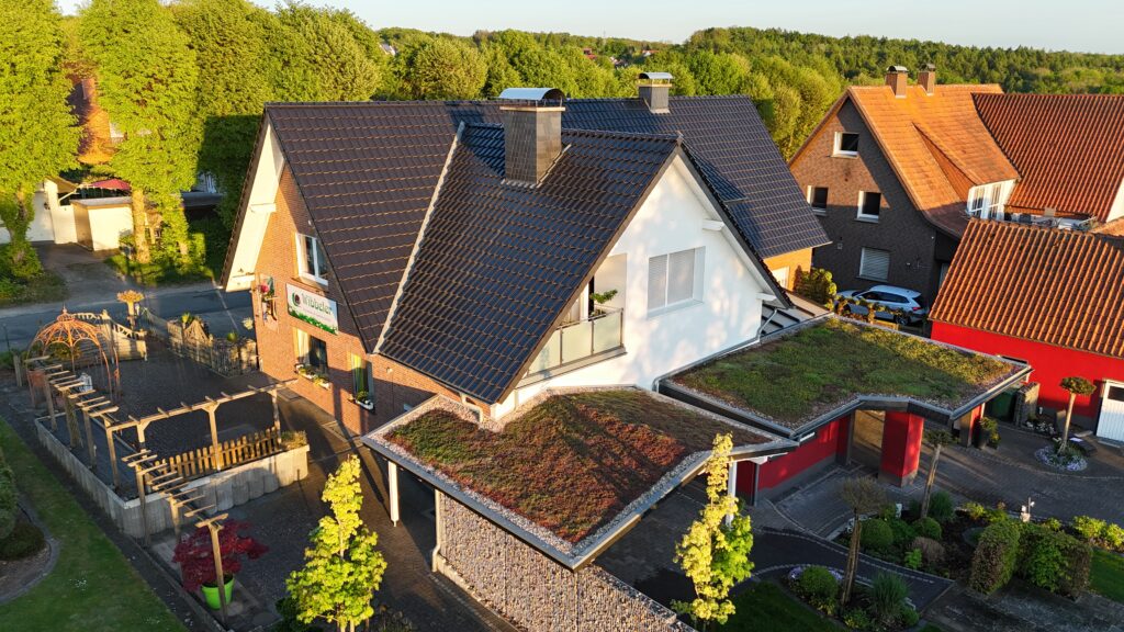 Vogelperspektive auf ein modernes Einfamilienhaus mit begrüntem Carport und gepflegtem Garten.