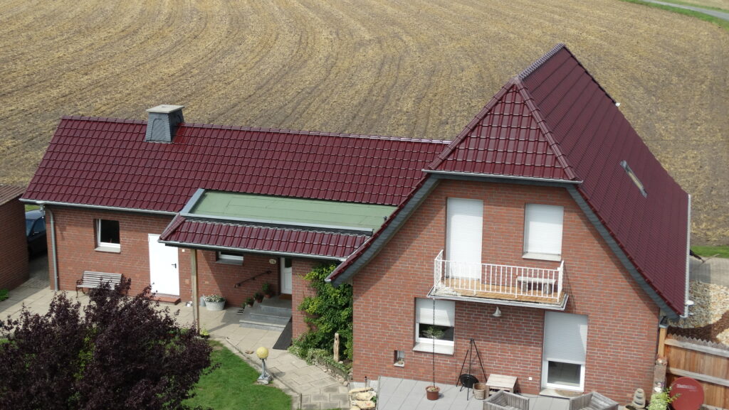 Ein rotes Ziegelhaus mit Balkon und Terrasse, umgeben von grünem Garten und ländlicher Landschaft.