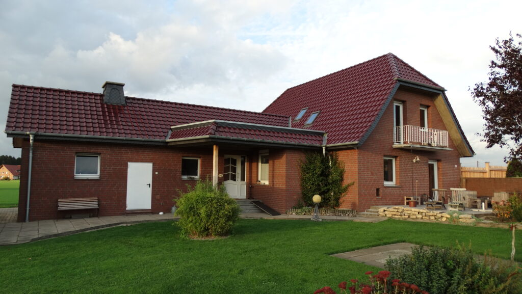Ein rotes Ziegelhaus mit Balkon, Terrasse und gepflegtem Garten in ländlicher Umgebung.