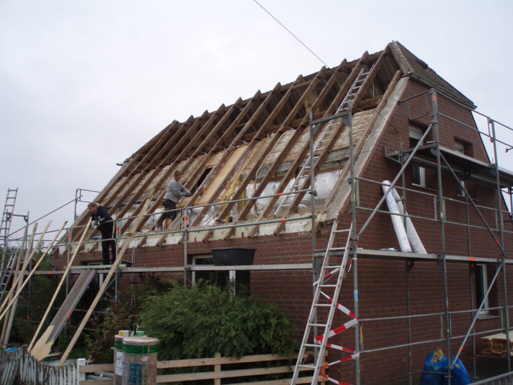 Ein zweistöckiges Backsteingebäude mit Gerüst; Arbeiter renovieren das Dach unter bewölktem Himmel.