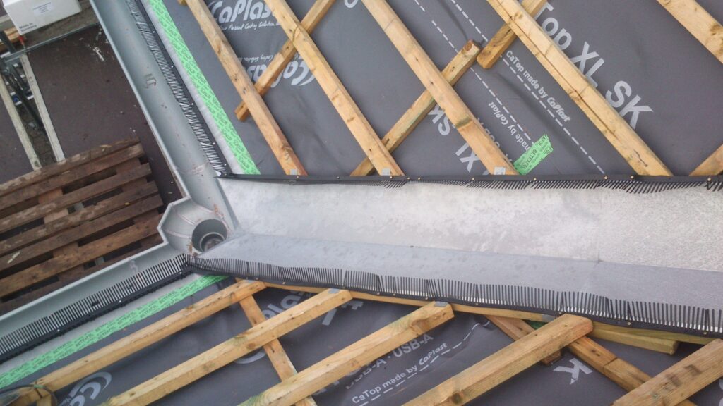 Baustelle eines Daches mit Holzbalken, Metall-Dachrinne und Schutzgitter, ohne Menschen oder Tiere.