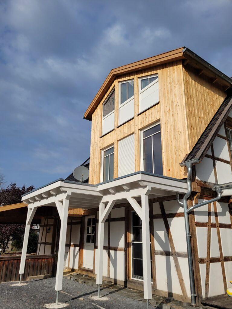 Ein zweistöckiges Fachwerkhaus mit modernen Holzelementen vor klarem, blauem Himmel.