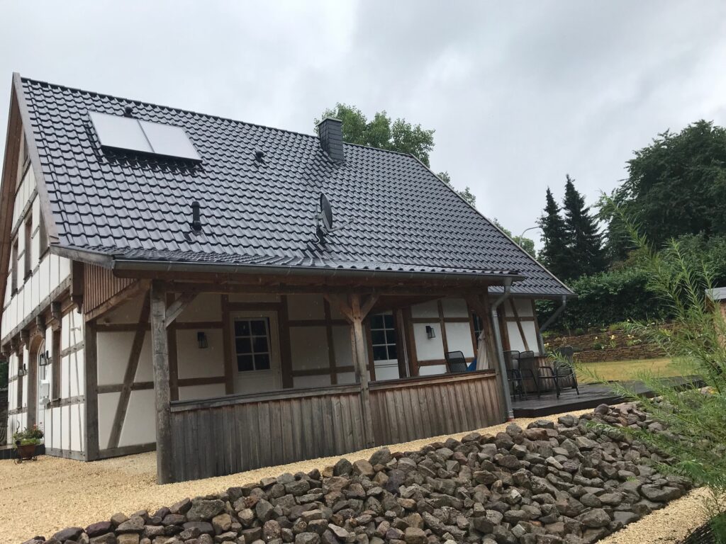 Traditionelles Fachwerkhaus mit Solarpaneelen auf dem Dach, umgeben von einem Steingarten.