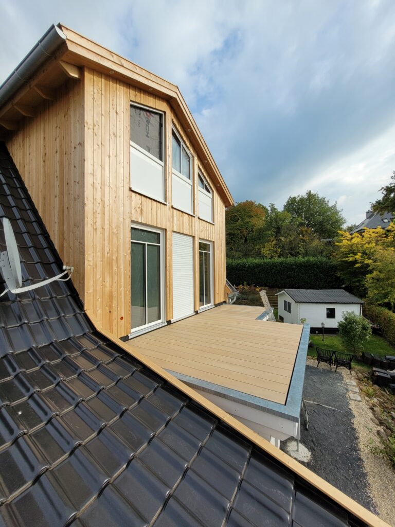 Modernes Haus mit Holzfassade, dunklem Dach, Terrasse und gepflegtem Garten in ruhiger Umgebung.