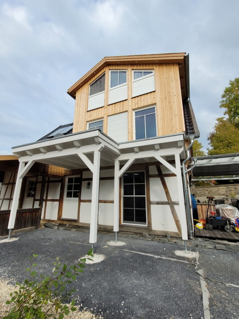 Modernes dreistöckiges Haus mit Holzfassade, weißen Akzenten und Fachwerk, in ruhiger Wohngegend.