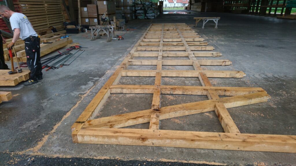 Ein Arbeiter bearbeitet eine große Holzkonstruktion in einer Werkstatt mit verschiedenen Werkzeugen.