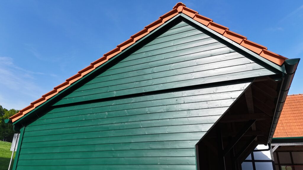 Ein traditionelles Gebäude mit grüner Holzfassade und orangefarbenem Ziegeldach unter klarem Himmel.