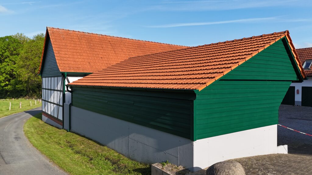 Traditionelles grünes Fachwerkhaus mit roten Ziegeldächern, umgeben von Rasen und blauer Himmel.