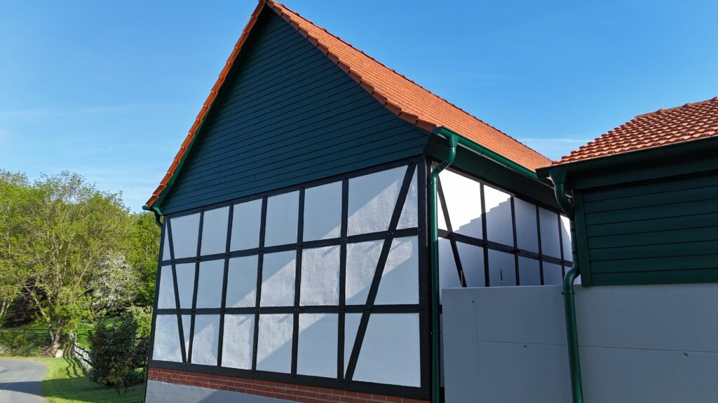 Fachwerkhaus mit modernem Anstrich, roten Ziegeln und grünen Dachrinnen vor klarem, blauem Himmel.