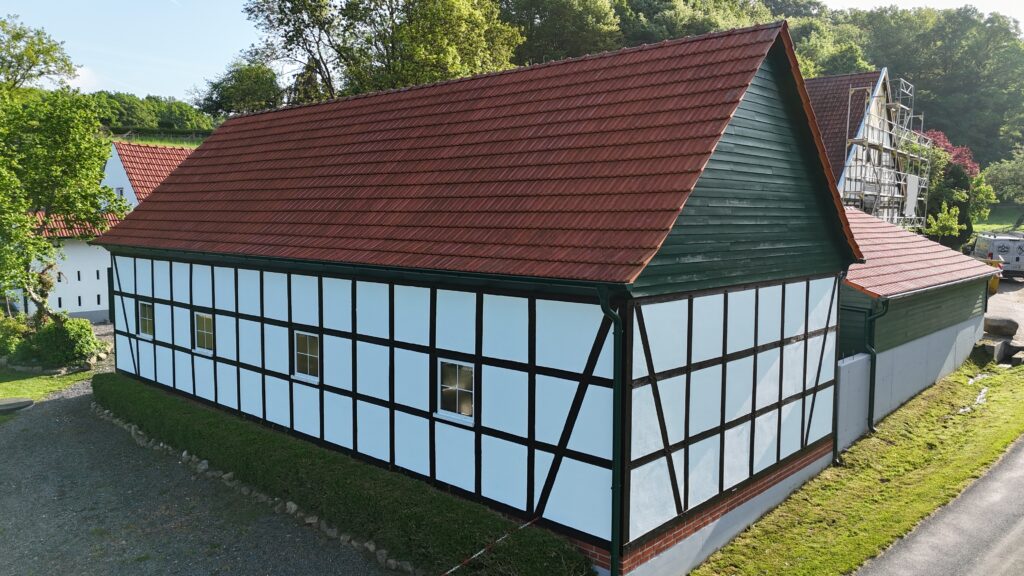 Ein traditionelles Fachwerkhaus mit rotem Ziegeldach in ländlicher Umgebung, Gerüst im Hintergrund.