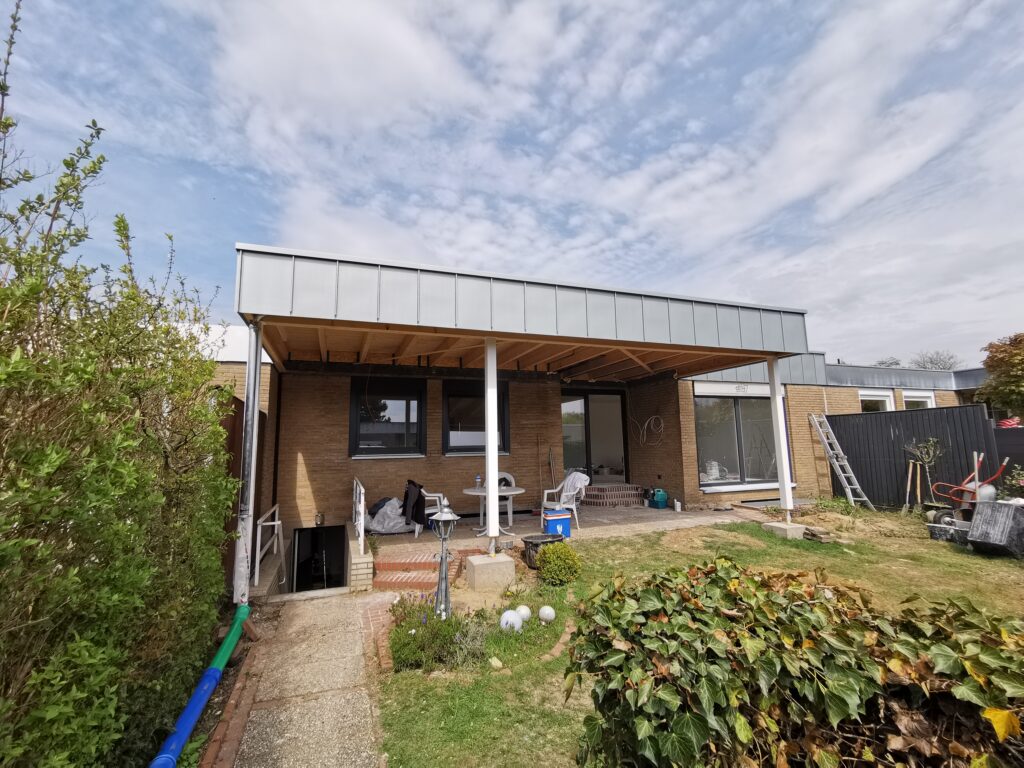 Moderne Hausrückseite mit überdachter Terrasse, Gartenmöbeln und Werkzeugen für Renovierungsarbeiten.