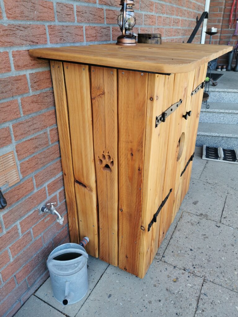 Rustikale Holzstruktur mit Bärenpfotenmotiv, Laterne oben, Gießkanne und Wasserhahn an Ziegelwand.