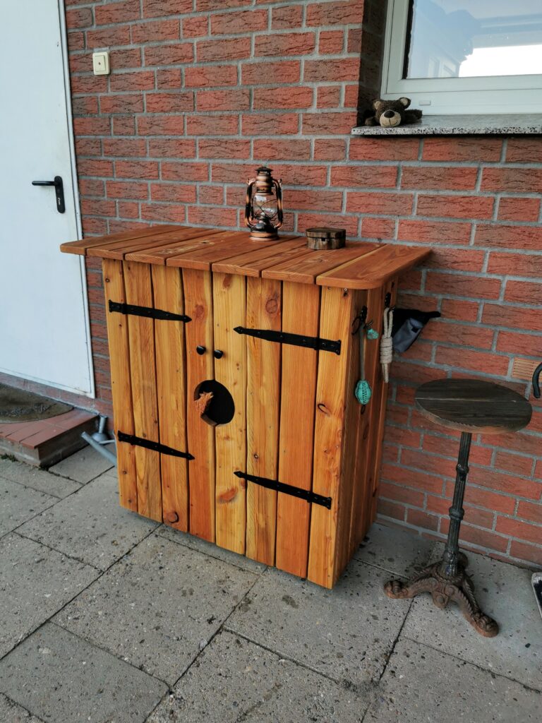 Ein rustikaler Holzschrank mit Laterne, Teddybär und Beistelltisch vor einer roten Backsteinwand.