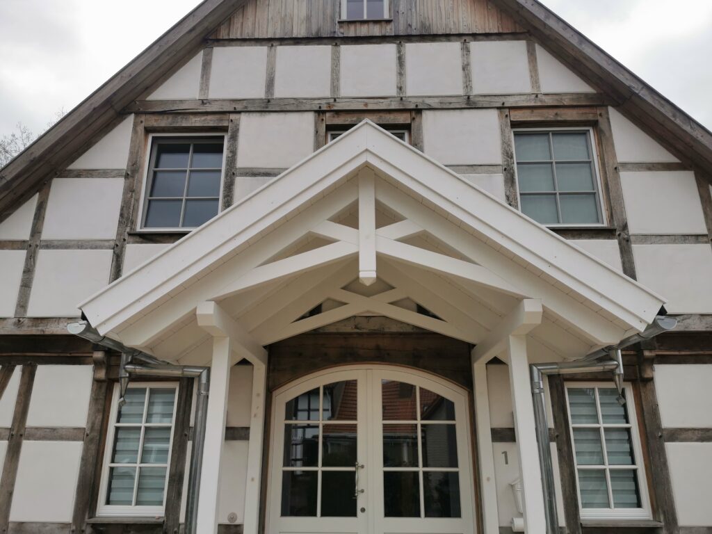 Fachwerkhaus mit weißer Fassade und dunklen Holzbalken, überdachter Eingang, traditionell und einladend.
