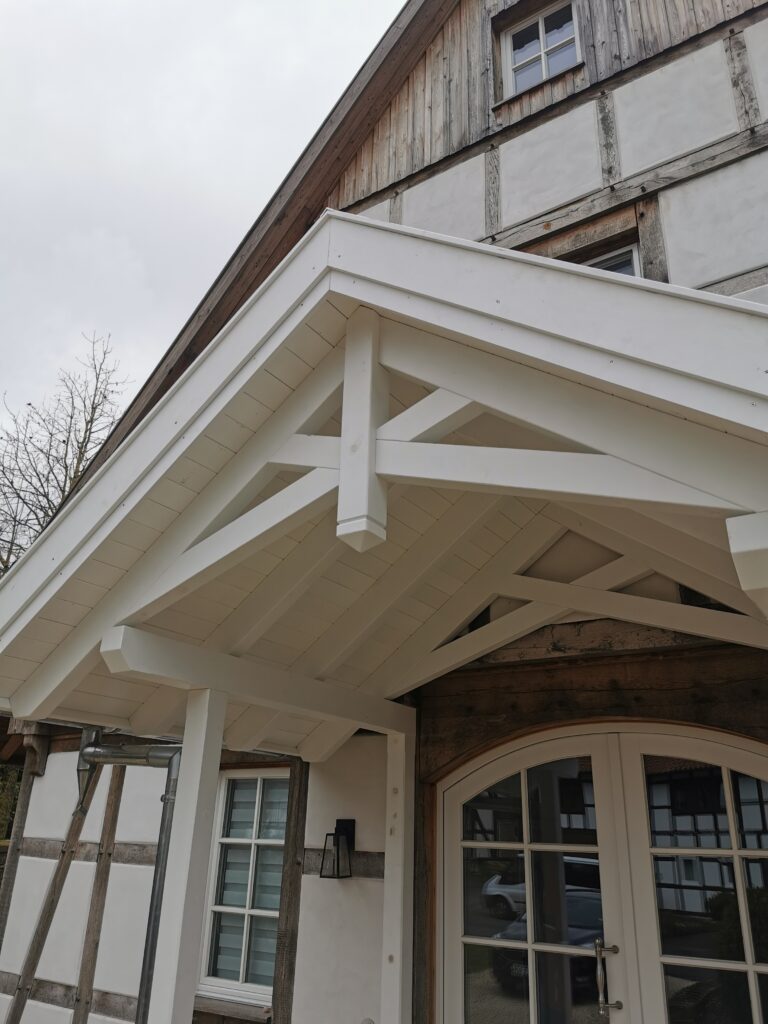 Fachwerkhaus mit weißem Vordach, rustikalen Holzbalken und Sprossenfenster, bei bewölktem Himmel.