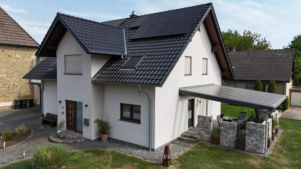 Modernes Einfamilienhaus mit Solarpaneelen auf dem Dach, umgeben von gepflegtem Garten.