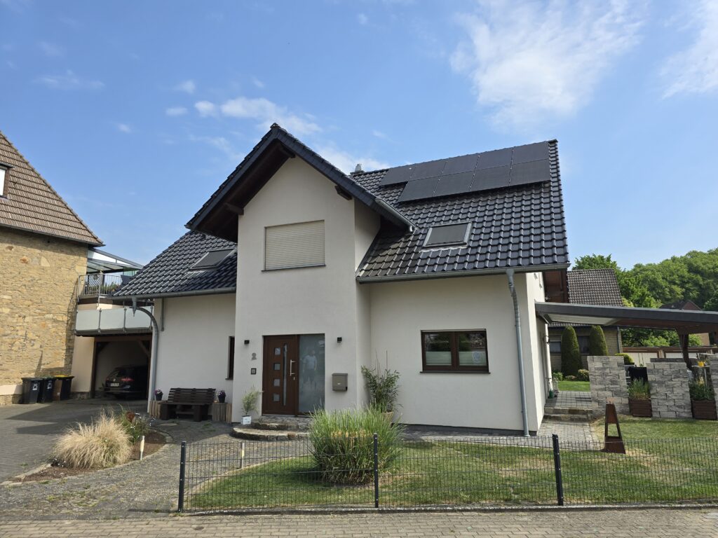 Modernes Einfamilienhaus mit Solardach, gepflegtem Vorgarten und gepflasterter Einfahrt in ruhiger Gegend.
