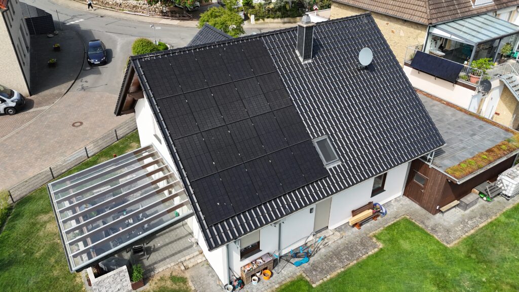 Vogelperspektive auf ein modernes Haus mit Solarpaneelen, Garten und überdachter Terrasse.