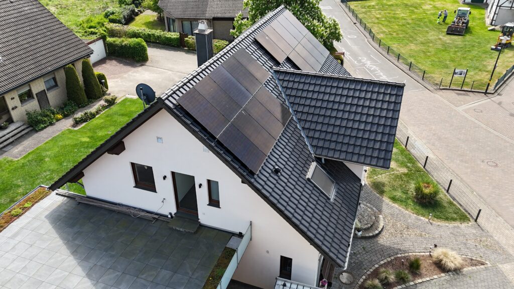 Luftaufnahme eines modernen Hauses mit Solarpanels auf dem Dach, umgeben von einem gepflegten Garten.