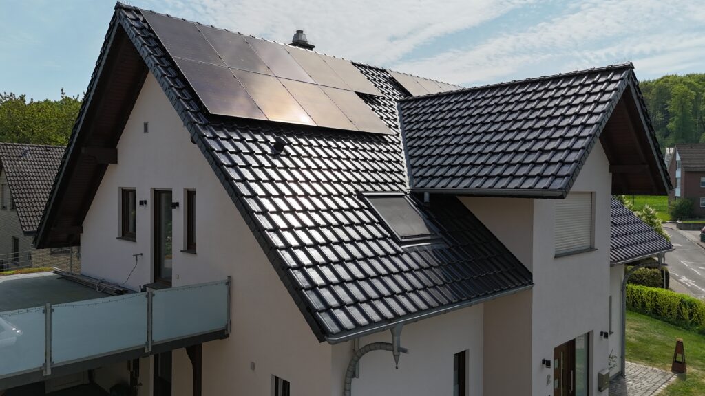 Modernes zweistöckiges Haus mit Solarpaneelen auf dem Dach, umgeben von einer grünen Umgebung.