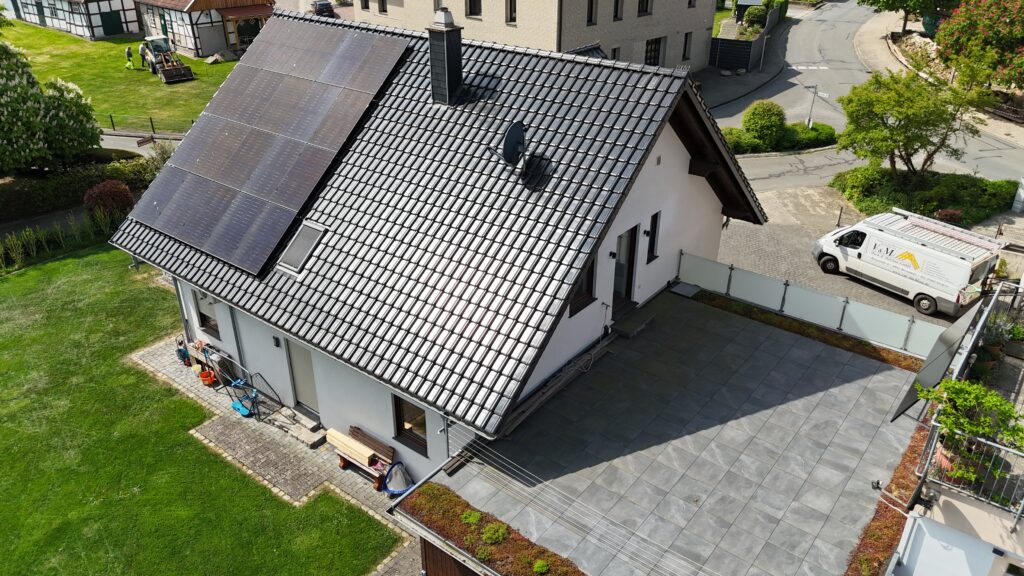 Vogelperspektive auf ein modernes Einfamilienhaus mit Solarpanels, gepflegtem Garten und Lieferwagen.