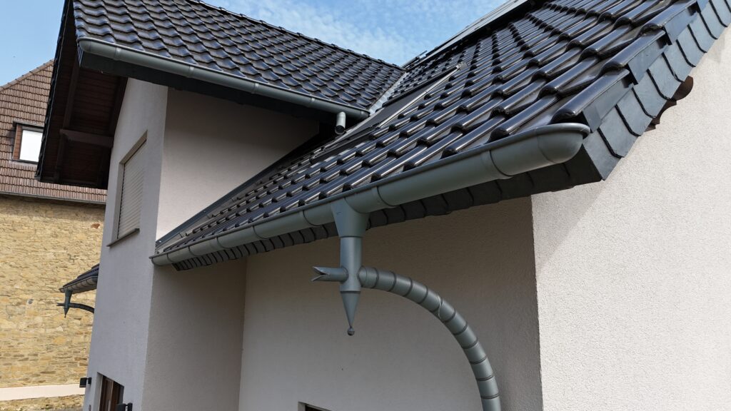 Modernes Hausdach mit dunkelgrauen Ziegeln und dekorativer Regenrinne in Drachenkopfform.
