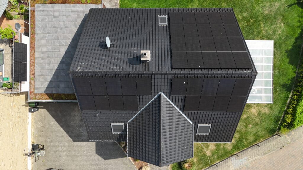 Moderne Vogelperspektive: Haus mit dunklem Dach, Solarpanelen, Schornstein und Satellitenschüssel.