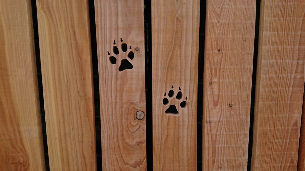 Holzwand mit zwei ausgeschnittenen Pfotenabdrücken, die eine rustikale und natürliche Atmosphäre schaffen.