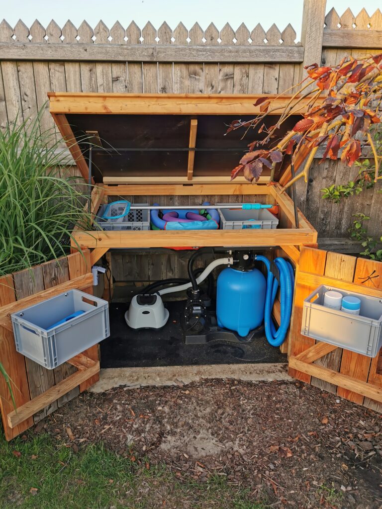 Offener Holzschuppen mit Poolzubehör, darunter Plastikboxen und ein blauer Poolfilter, im Garten.