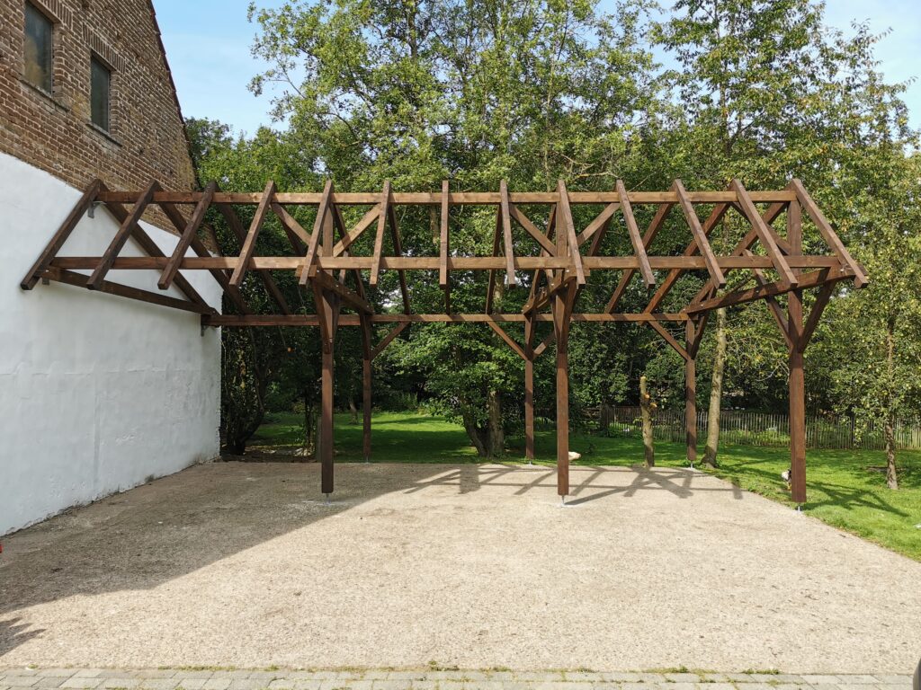 Holzunterstand an weißer Wand, umgeben von grünen Bäumen und Gras, mit ländlicher, ruhiger Atmosphäre.
