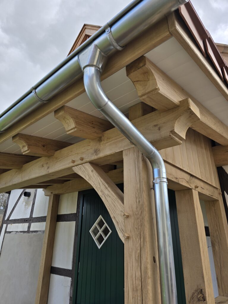 Fachwerkhaus mit grüner Tür und moderner Dachrinne; traditionelle und moderne Elemente vereint.